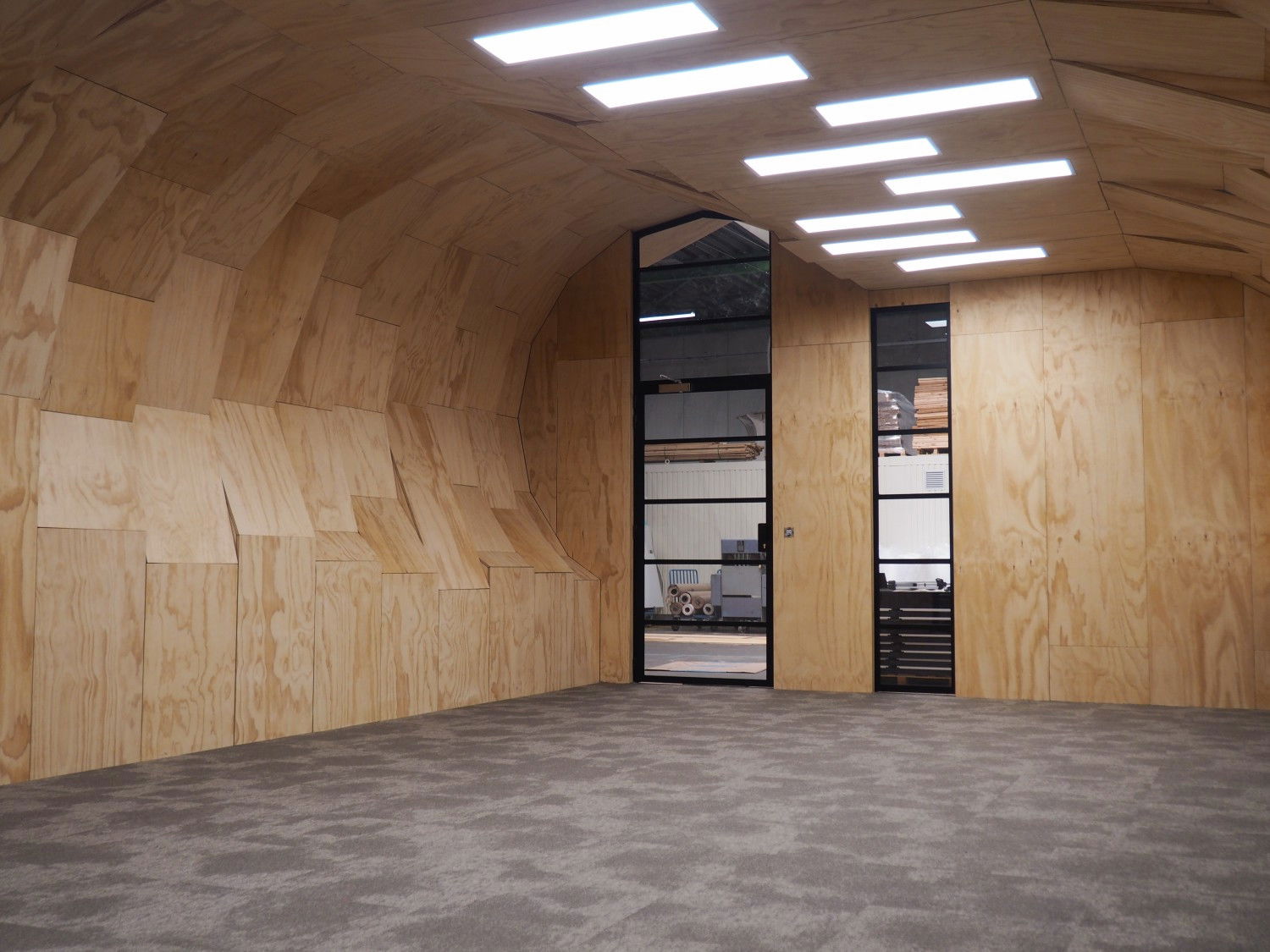Inside the unit looking at the left entrace door from the opposite right corner. Floors have a random, cloudy gray pattern, the ceiling features a series of  randomly placed led panels.