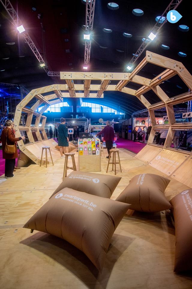 Inside the right side looking through the structure. In the front, a group of inflated paper cushions; at the centre, a counter with flyer samples, computers and bar stools.