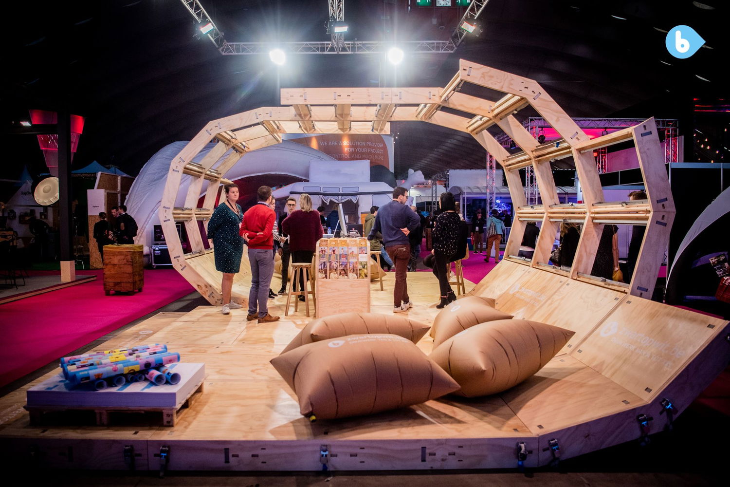 Looking from the right side through the structure. In the front, a group of inflated paper cushions; at the centre, a group of people chatting.